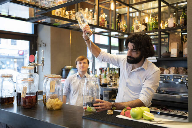 Männlicher Barkeeper schüttet an Theke Alkohol in Fruchtglas — Stockfoto