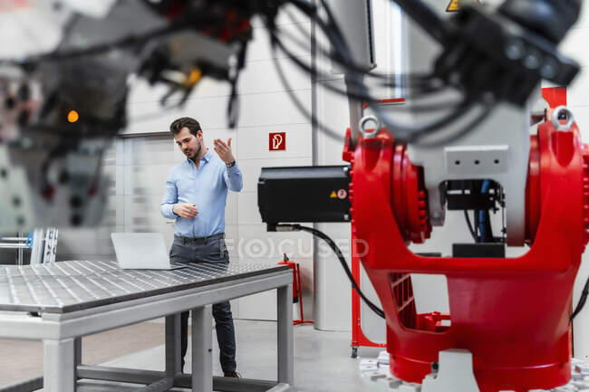 Young male entrepreneur discussing during video conference through laptop while machinery in foreground at factory — Stock Photo