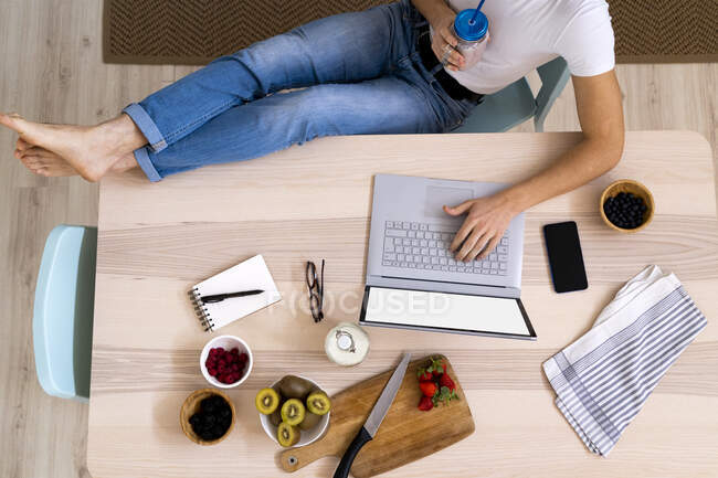 Man holding smoothie jar while using laptop sitting at table in kitchen — Stock Photo