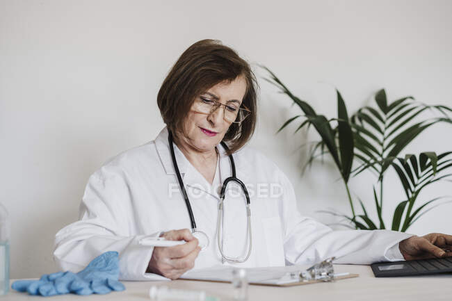 Senior rapporto di lettura medico femminile mentre seduto alla scrivania in clinica — Foto stock