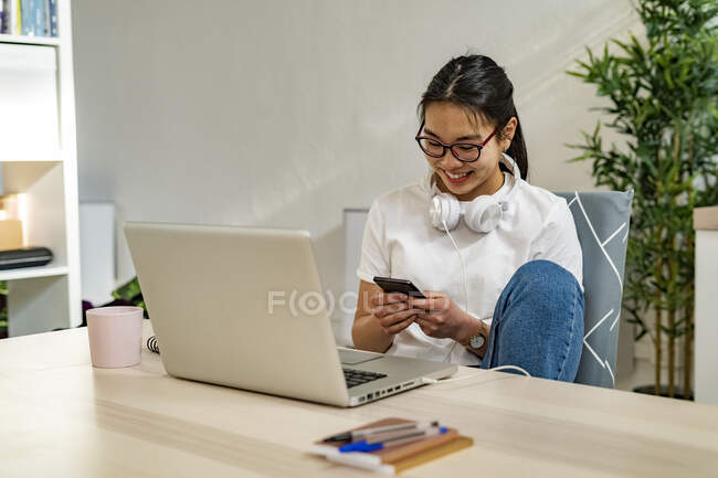 Jeune femme utilisant un téléphone portable tout en étant assis avec ordinateur portable à la maison — Photo de stock