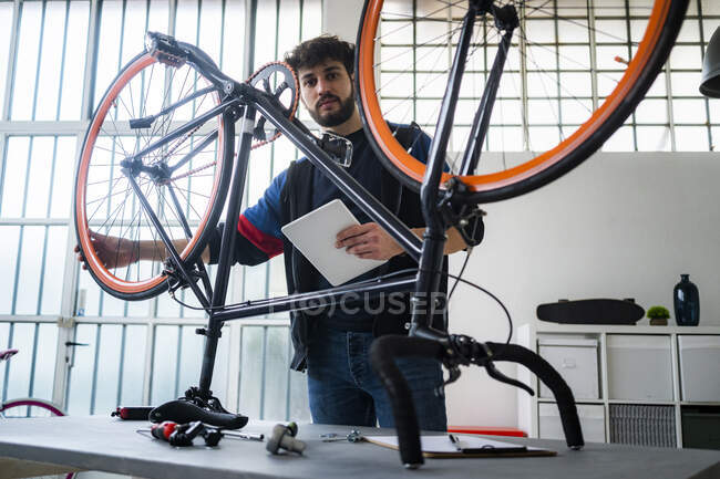 Homme avec tablette numérique tenant roue de vélo à la maison — Photo de stock