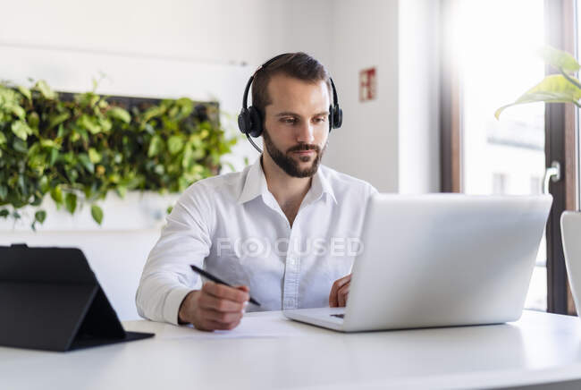 Entrepreneur avec écouteurs travaillant sur ordinateur portable au bureau — Photo de stock