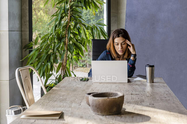 Besorgte Geschäftsfrau benutzt Laptop, während sie am Konferenztisch im Büro sitzt — Stockfoto