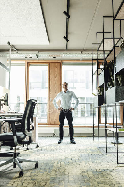 Бізнесмен з рукою на стегно стоїть проти скла в офісі — стокове фото