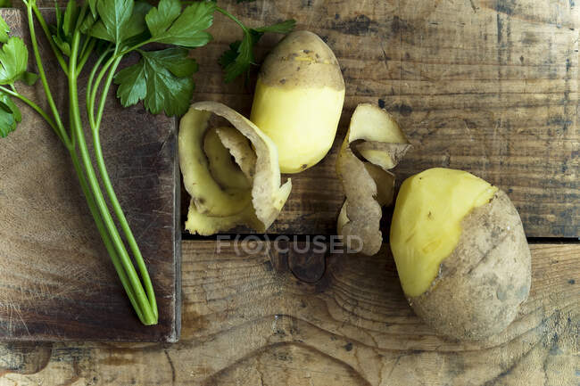 Half peeled potatoes and parsley leaves on rustic wooden background — Stock Photo