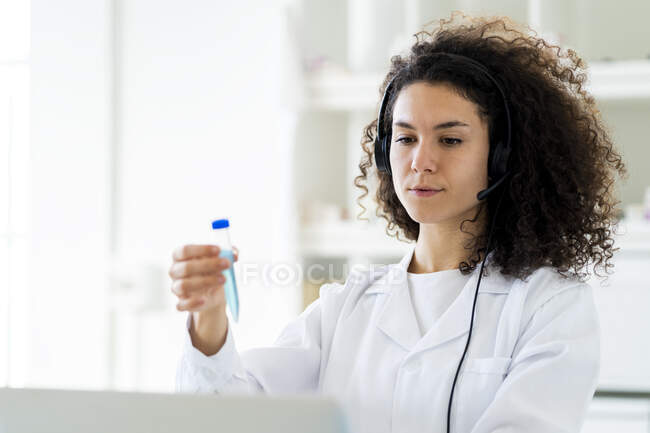 Doctora con tubo de ensayo con auriculares mientras trabaja en el hospital - foto de stock
