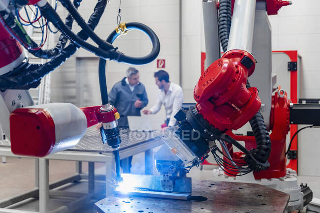 Роботизированная сварка рук во время обсуждения инженерами-мужчинами на заводе — стоковое фото