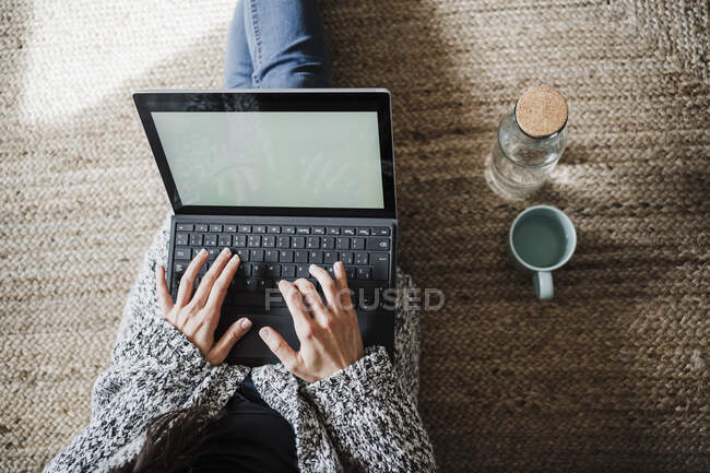 Frau benutzt Laptop, während sie zu Hause auf Jute sitzt — Stockfoto