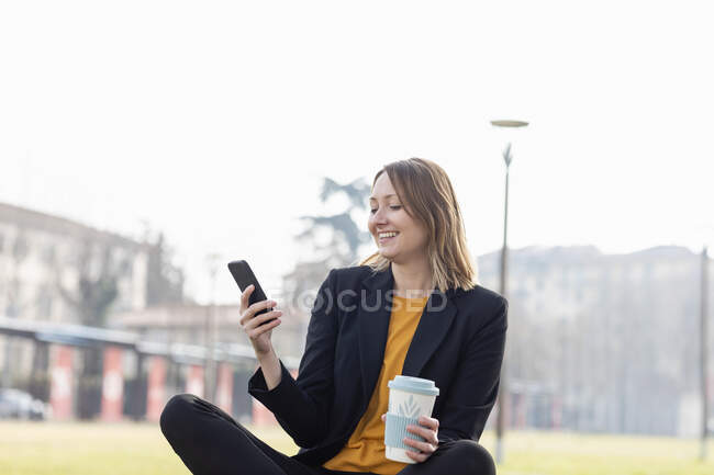 Усміхнений підприємець з одноразовою чашкою за допомогою мобільного телефону — стокове фото