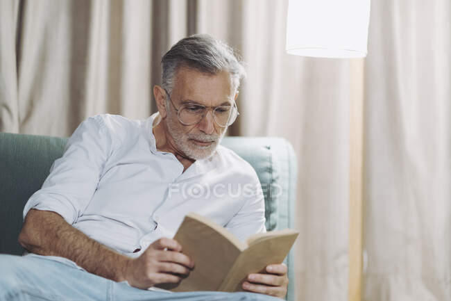 Любопытный человек читает книгу, сидя на диване в номере отеля — стоковое фото