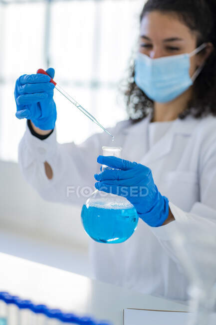 Médico femenino analizando solución en vaso de precipitados en laboratorio de química - foto de stock