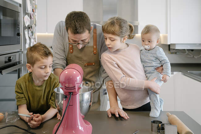 Father and children looking at stand mixer in kitchen — Stock Photo