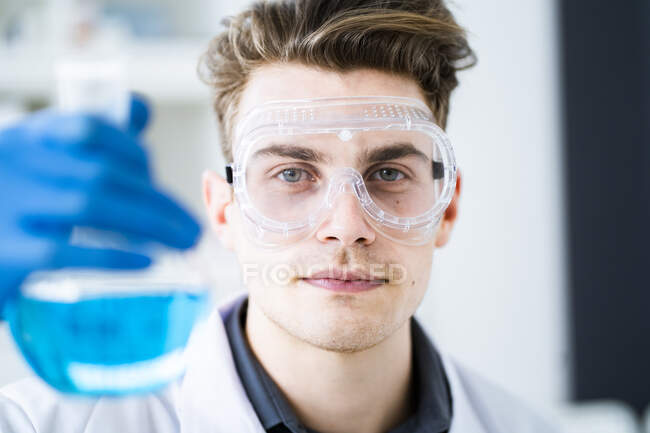 Молодий науковець носить захисні окуляри, а в лабораторії тримає колбу з хімічними речовинами. — стокове фото