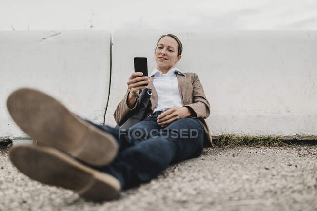 Filet de surf femme d'affaires détendu tout en étant assis à la barrière de crash sur le bord de la route — Photo de stock