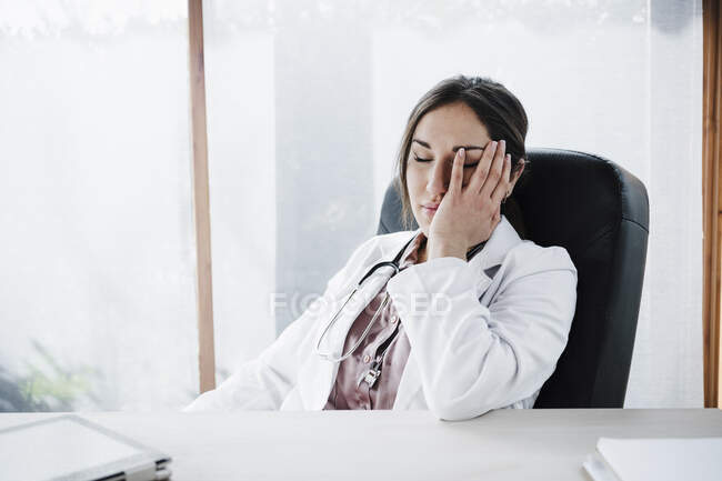 Tired female doctor with eyes closed sitting at desk — Stock Photo