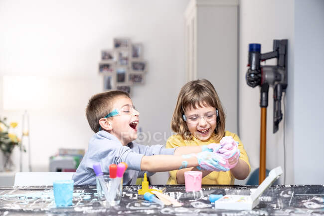 Allegro fratello e sorella con melma sulle mani che giocano a tavola — Foto stock