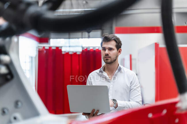 Male engineer with laptop seen through robotics in factory — Stock Photo