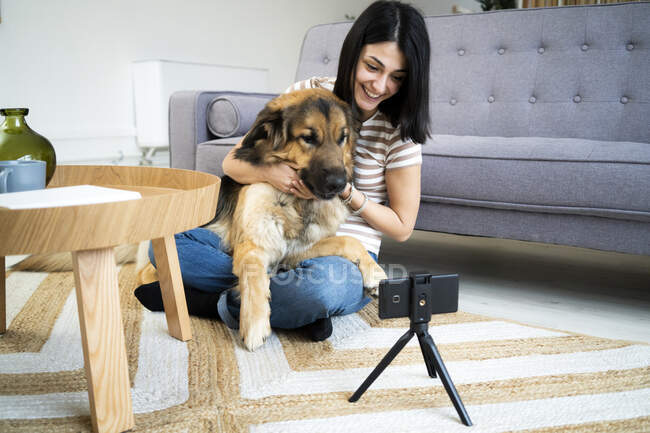 Mulher sorridente com cão vlogging através de telefone inteligente em casa — Fotografia de Stock