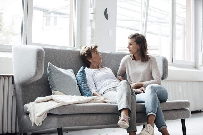 Relajada mujer mayor hablando con su nieta mientras está sentada en el sofá en casa - foto de stock