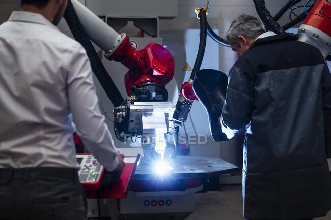 Male welder examining robotics while standing by young engineer working in factory — Stock Photo