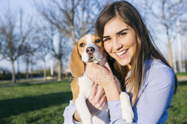Propietaria de mascotas sonriendo mientras abraza al perro en el parque - foto de stock