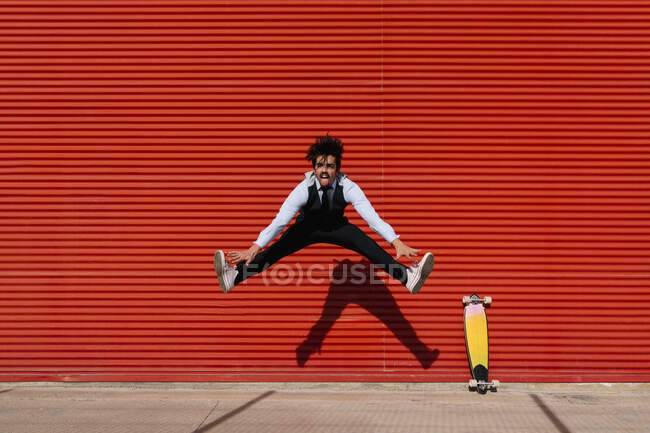 Hombre de negocios juguetón saltando en monopatín contra la pared - foto de stock