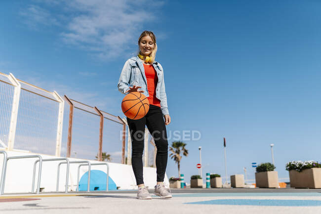 Donna sorridente che gioca con il basket a terra contro il cielo — Foto stock