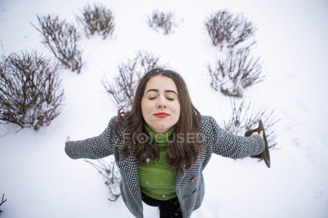 Mulher bonita com braços estendidos segurando chapéu em terra coberta de neve durante o inverno — Fotografia de Stock