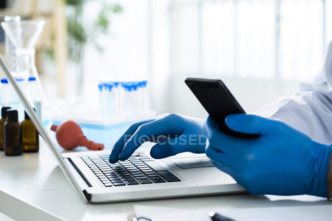 Scientist holding smart phone while using laptop at desk in laboratory — Stock Photo