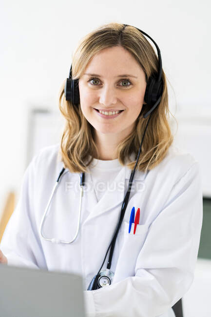 Усмішка жінка-медик у навушниках під час онлайн-консультації в медичній клініці — стокове фото
