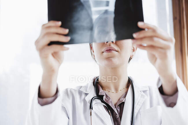 Femme médecin professionnel examinant l'image radiographique contre fenêtre — Photo de stock