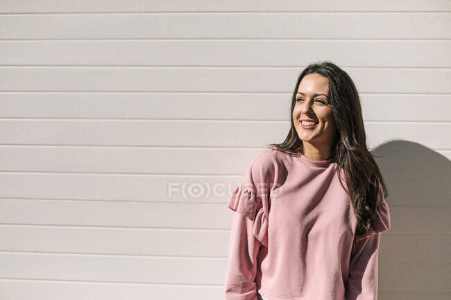 Donna sorridente guardando lontano mentre in piedi contro il muro durante la giornata di sole — Foto stock