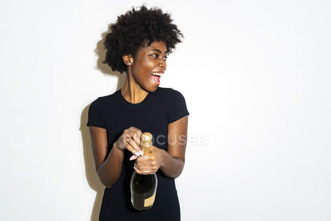 Donna felice guardando lontano mentre apriva bottiglia di champagne in piedi sullo sfondo bianco — Foto stock