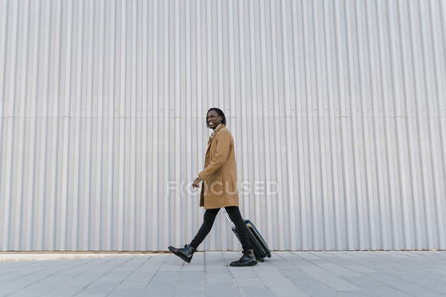 Smiling man walking with suitcase against gray wall — Stock Photo