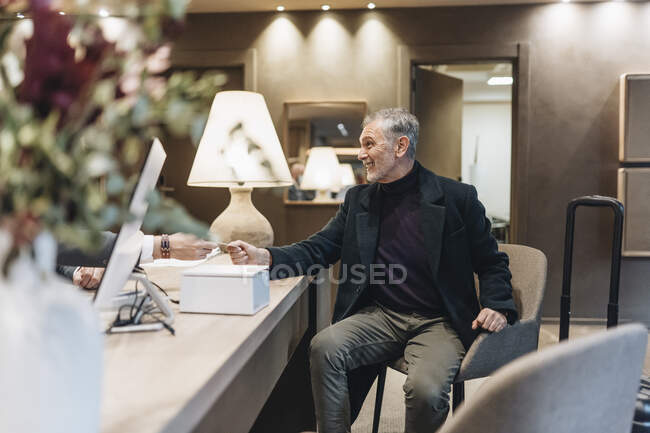 Smiling mature man taking cardkey from hotel reception — Stock Photo