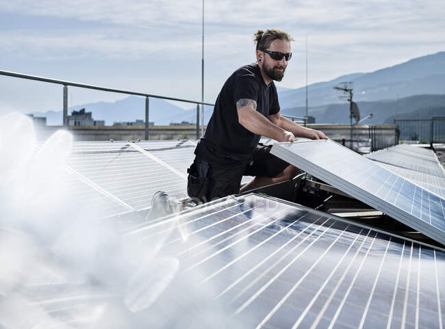 Electricista masculino instalando paneles solares en la terraza del edificio durante el día soleado - foto de stock
