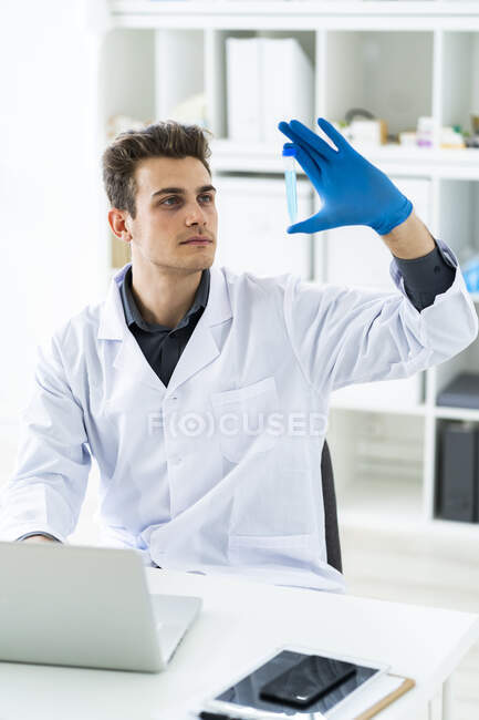 Científico masculino concentrado examinando líquido en tubo de ensayo mientras usa computadora portátil en laboratorio - foto de stock