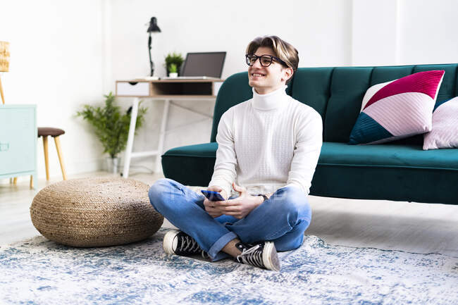 Happy man sitting on carpet in living room looking away — Stock Photo