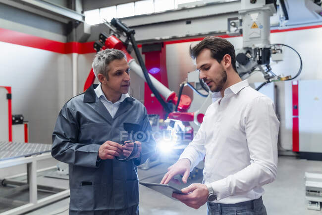 Jeune ingénieur masculin utilisant une tablette numérique tout en discutant avec l'homme mûr dans l'usine — Photo de stock