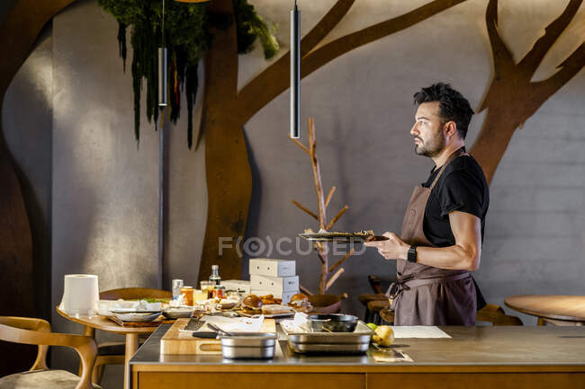 Продуманий чоловічий шеф-кухар тримає харчову тарілку на сучасній кухні — стокове фото