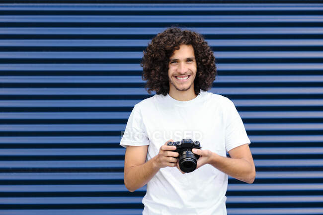 Curly homem de cabelos compridos segurando câmera enquanto estava em frente ao obturador fechado — Fotografia de Stock