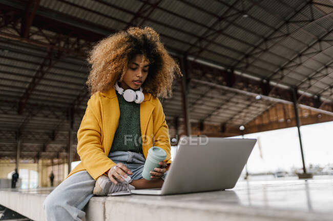 Афро женщина с одноразовой чашки кофе с помощью ноутбука в гостиной — стоковое фото