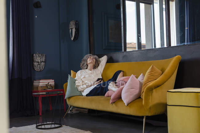 Femme âgée avec tablette numérique se détendre sur le canapé à la maison — Photo de stock