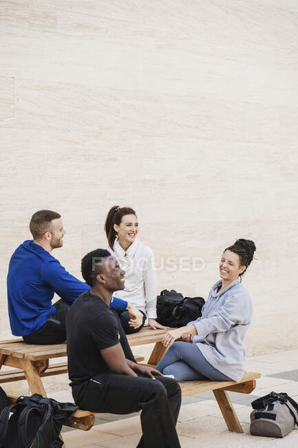 Multi-ethnische Gruppe von Athleten lacht, während sie auf Bank sitzt — Stockfoto