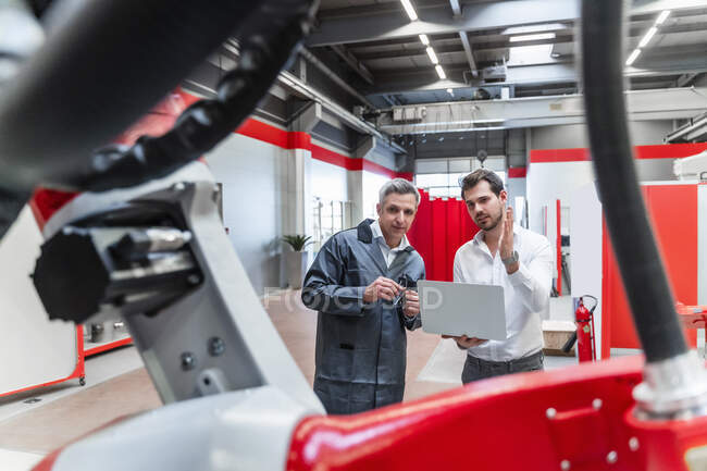 Инженеры-мужчины с ноутбуком обсуждают робототехнику в промышленности — стоковое фото
