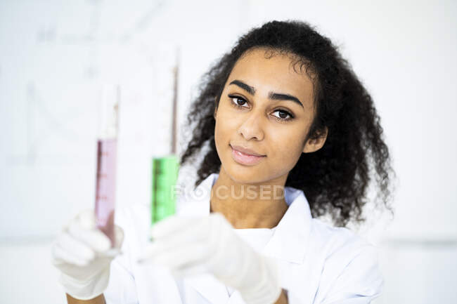 Joven investigadora sosteniendo tubos de ensayo con líquido en laboratorio - foto de stock