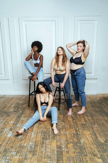 Gruppo multietnico di donne che indossano reggiseni e jeans in posa contro il muro — Foto stock