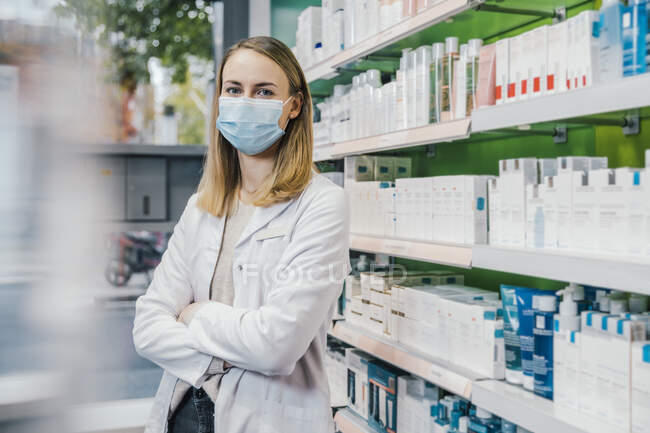 Farmacêutico com braços cruzados usando máscara protetora na farmácia — Fotografia de Stock