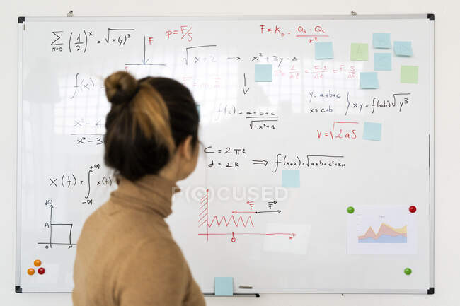 Femme analysant la formule mathématique écrite sur tableau blanc dans le salon — Photo de stock